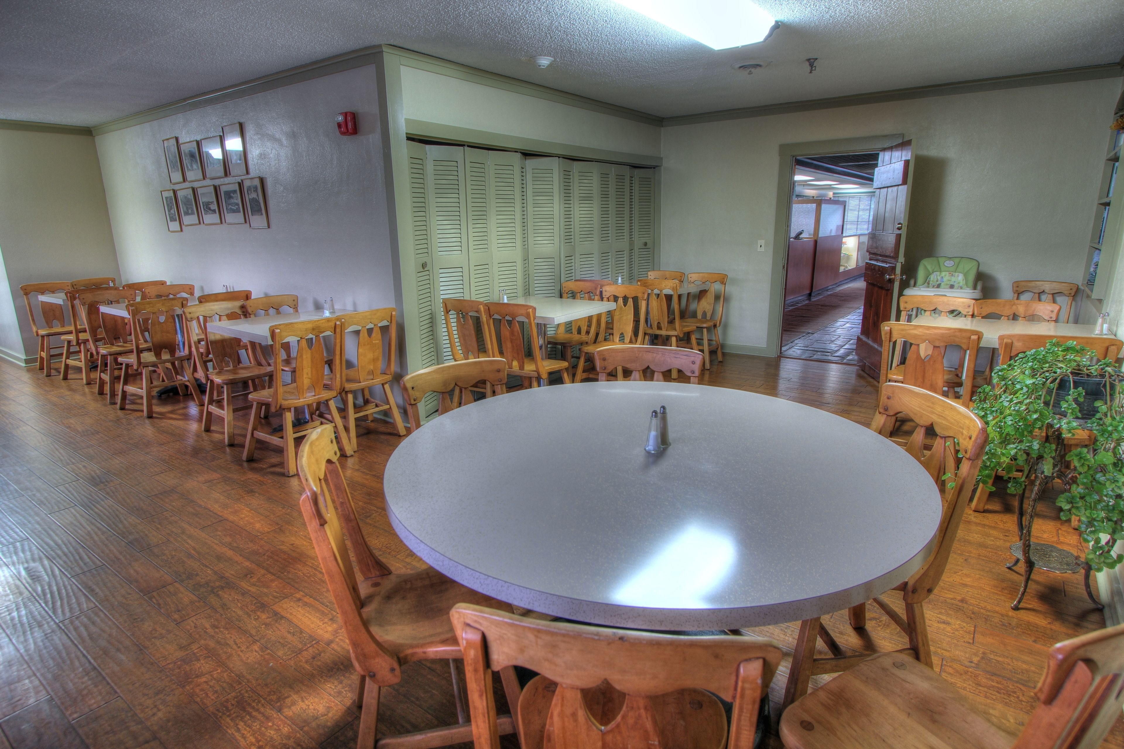 A dining area with wooden tables and chairs, a round table in the center, and a hallway leading to another room.