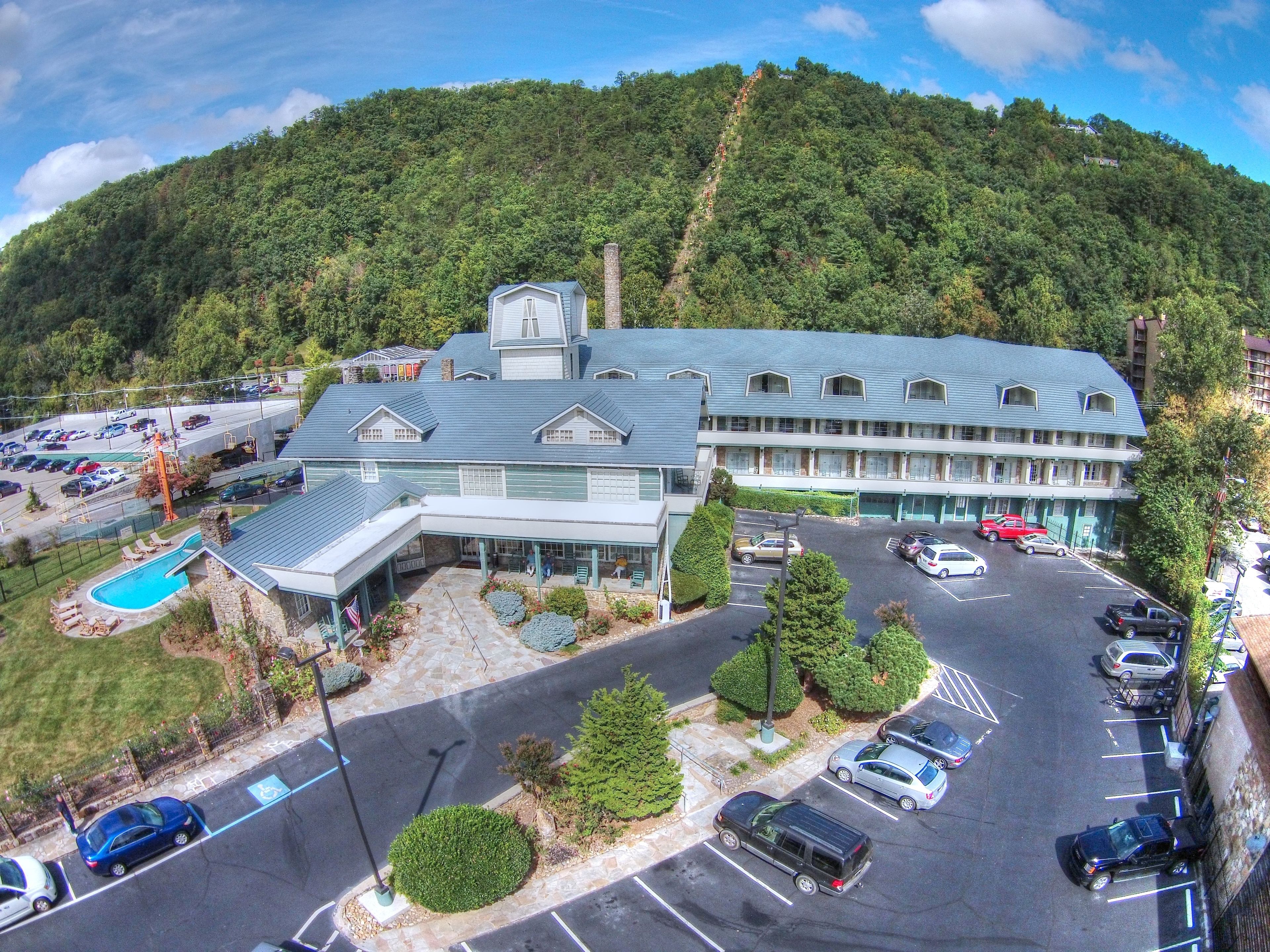 A hotel with a pool, parking lot, and a view of a forested hill.