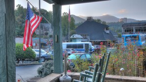 A view from a porch with a stone bench, American flags, a parking lot with cars, and a mountain in the background.