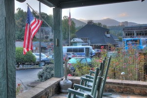 A view from a porch with a stone bench, American flags, a parking lot with cars, and a mountain in the background.