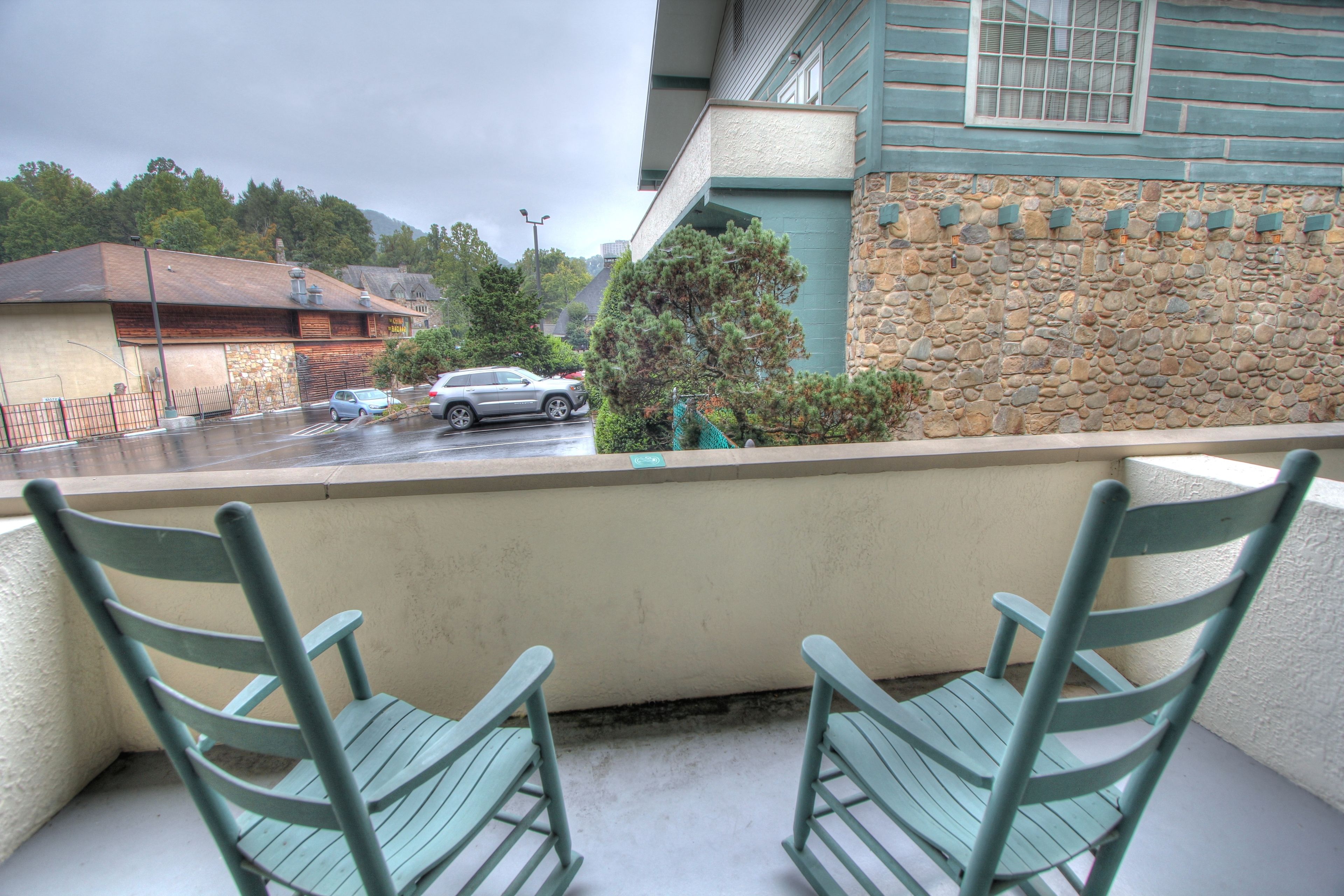 A balcony with two green chairs, a stone wall, and a view of a street with cars and buildings.