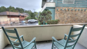 A balcony with two green chairs, a stone wall, and a view of a street with cars and buildings.