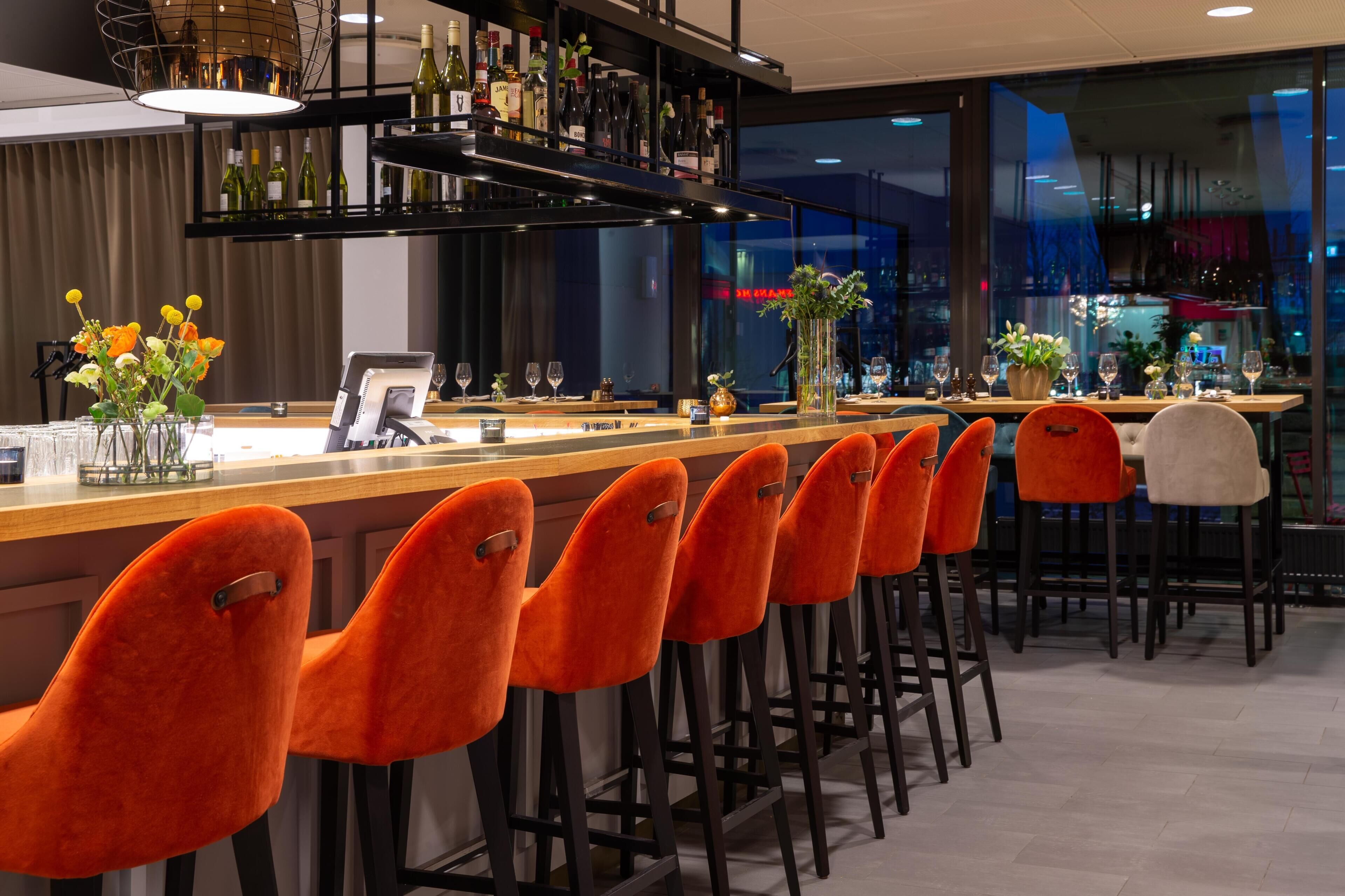 A bar area with a long counter, multiple wine bottles, and a variety of glasses.