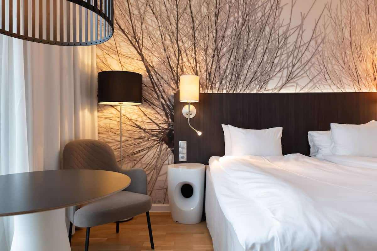Una habitación de hotel moderna con cama, una silla, una mesa y una lámpara.