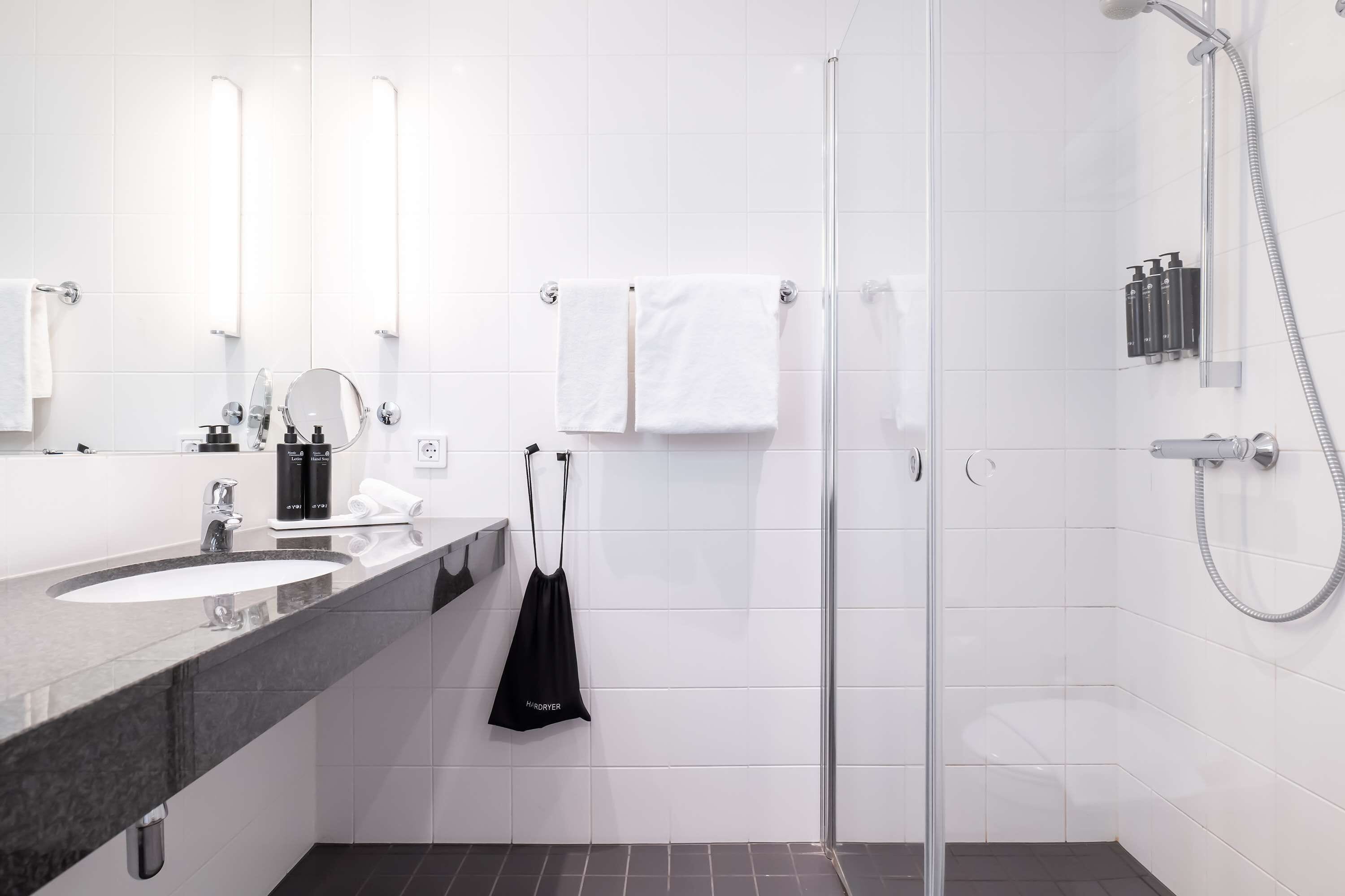 Un baño moderno con un espejo grande, dos lavamanos, una ducha y un perchero para toallas.