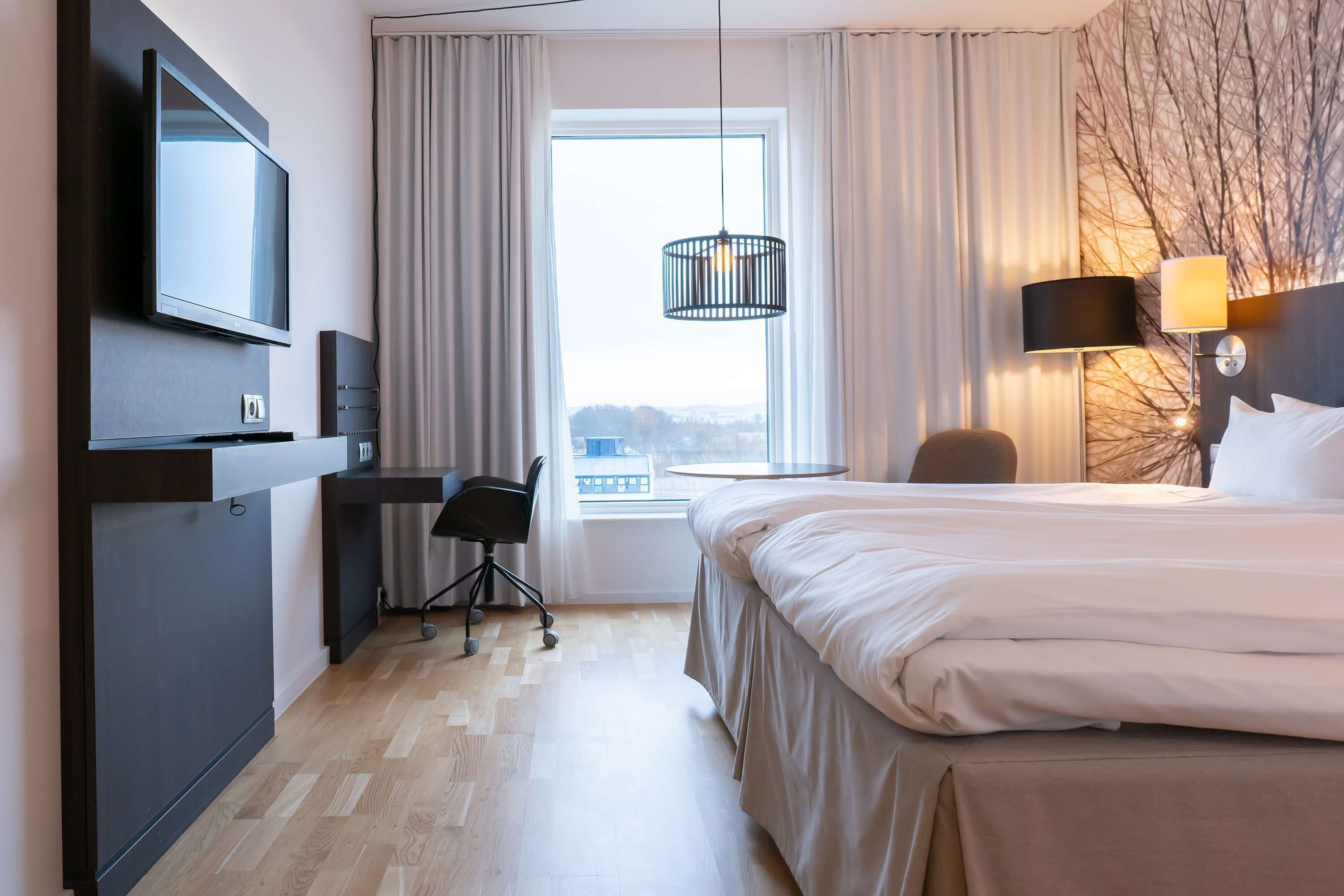 Habitación de hotel con cama, escritorio, silla, televisor y vistas al exterior.