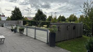 A rooftop terrace with a metal railing, potted plants, and a wooden structure.