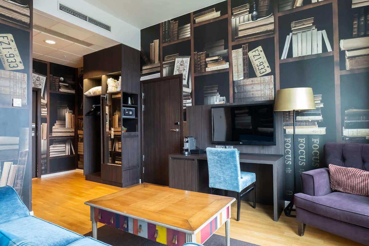 Una sala de estar moderna con una mesa de centro de madera, un sofá azul, un sofá púrpura, un escritorio con una silla y una estantería llena de libros.