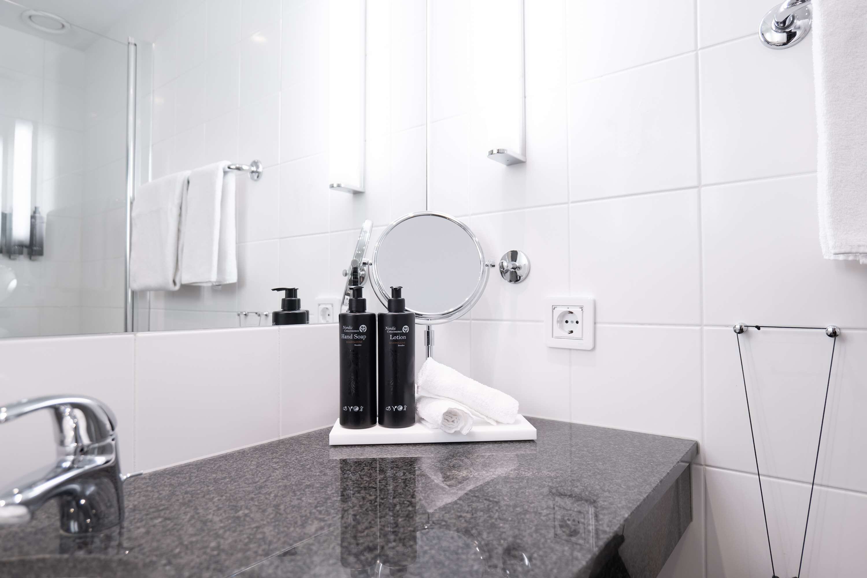 A modern bathroom with a granite countertop, a round mirror, and two bottles of hand soap and lotion.
