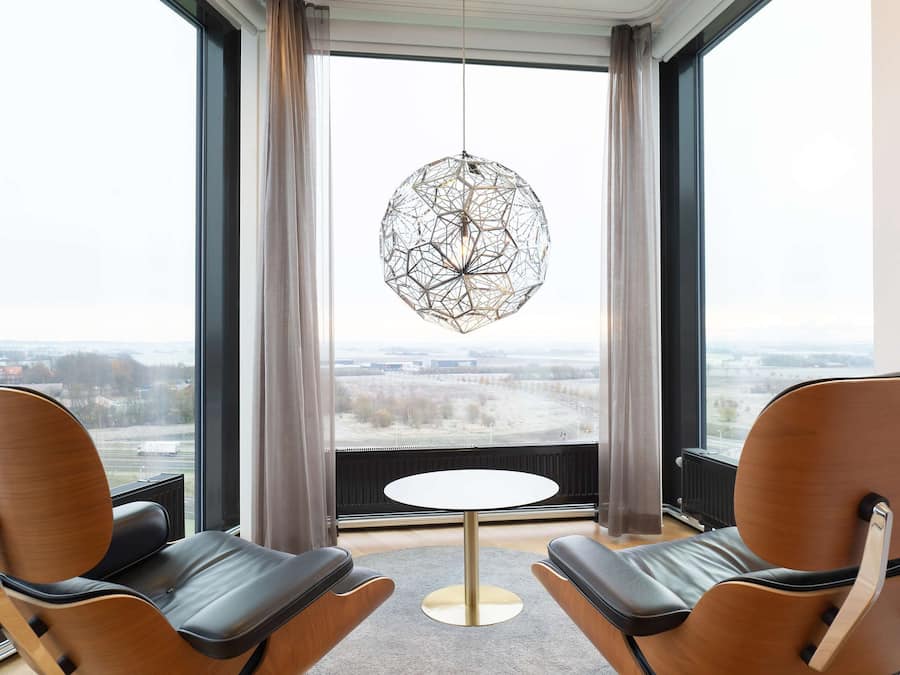 Una habitación moderna con dos sillones de cuero, una mesa redonda y una lámpara colgante geométrica original.