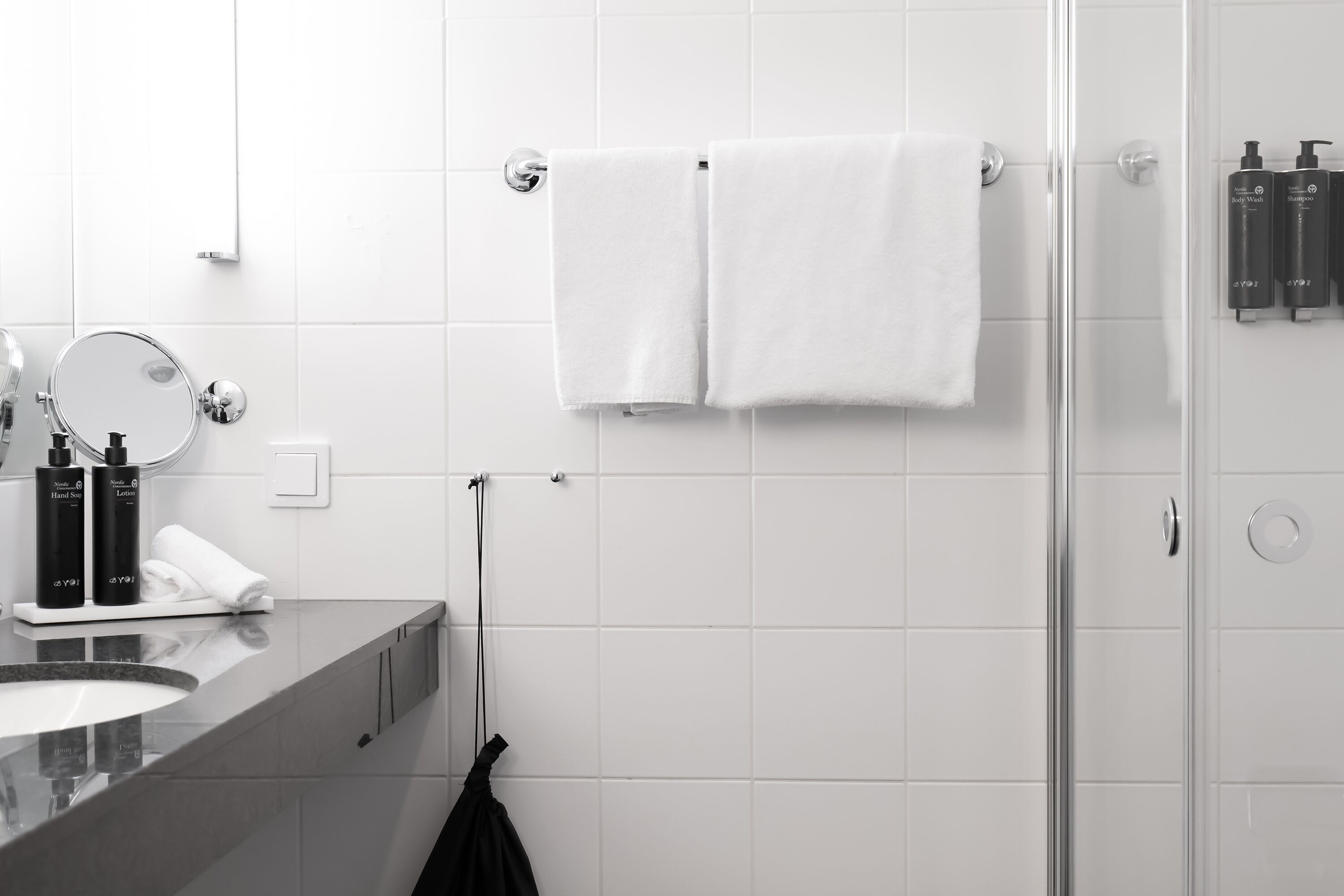 Een moderne badkamer met een douchecabine van glas, een witte handdoek aan een rek en toiletartikelen op het aanrecht.