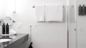 A modern bathroom with a glass shower enclosure, a white towel hanging on a rack, and toiletries on the countertop.