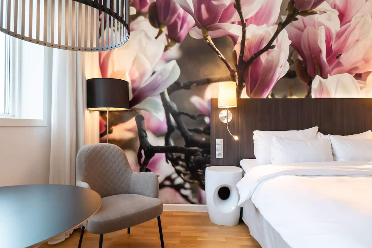 Habitación de hotel con cama, una silla, una mesa, una lámpara y una pared con un mural floral.