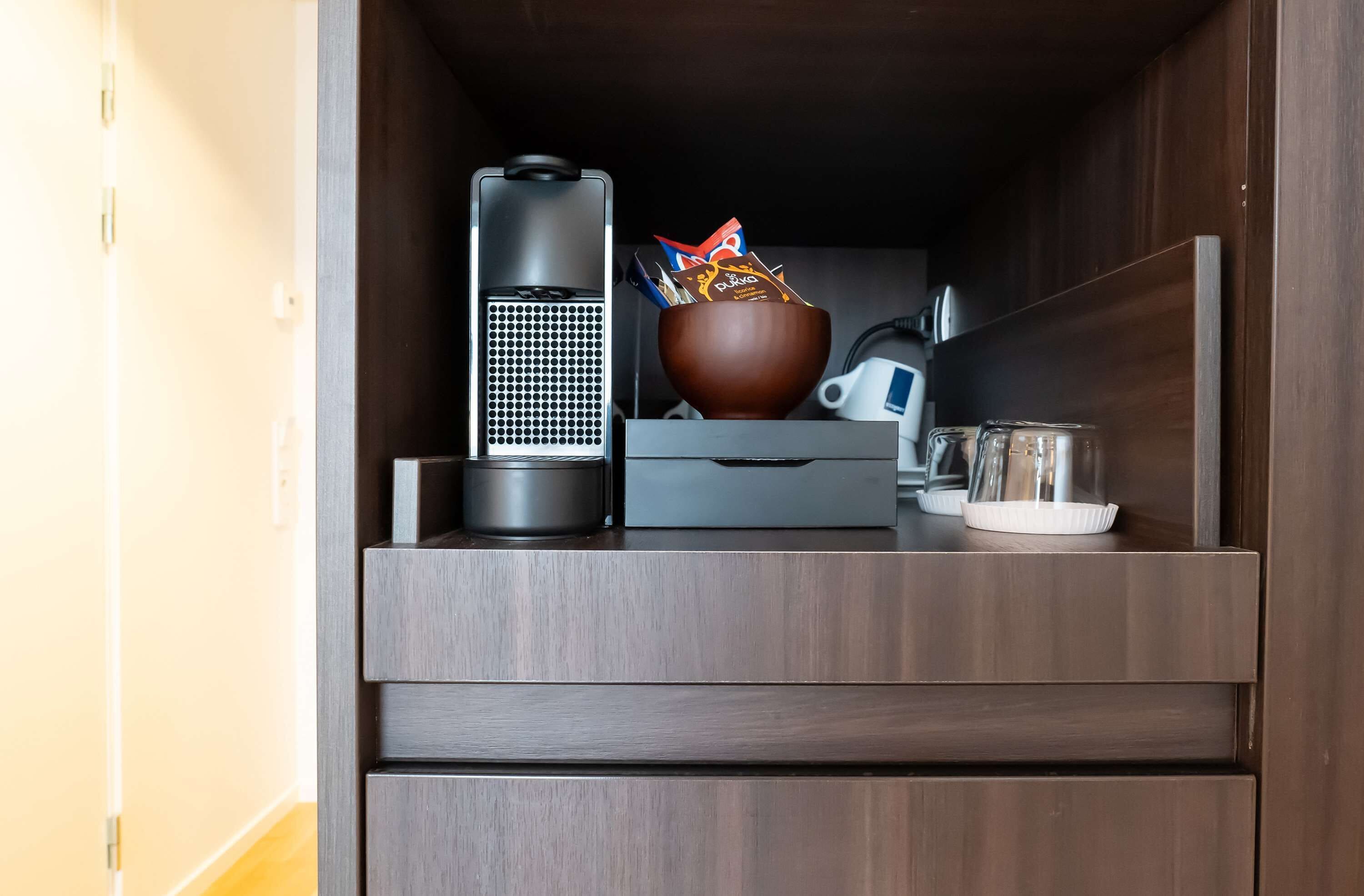 Une petite cuisine équipée d’une machine à café, d’une tasse, d’un bol contenant des en-cas et d’un récipient.