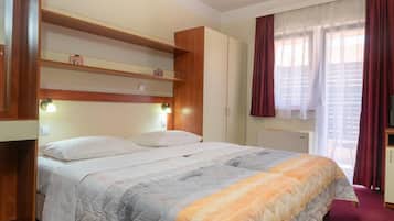 Un dormitorio con cama, cabecera de madera, estanterías empotradas, armario y ventana con cortinas.