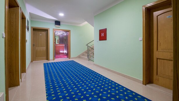 Een hal met een blauw gestreept tapijt, houten deuren en een trap die naar een lift leidt.