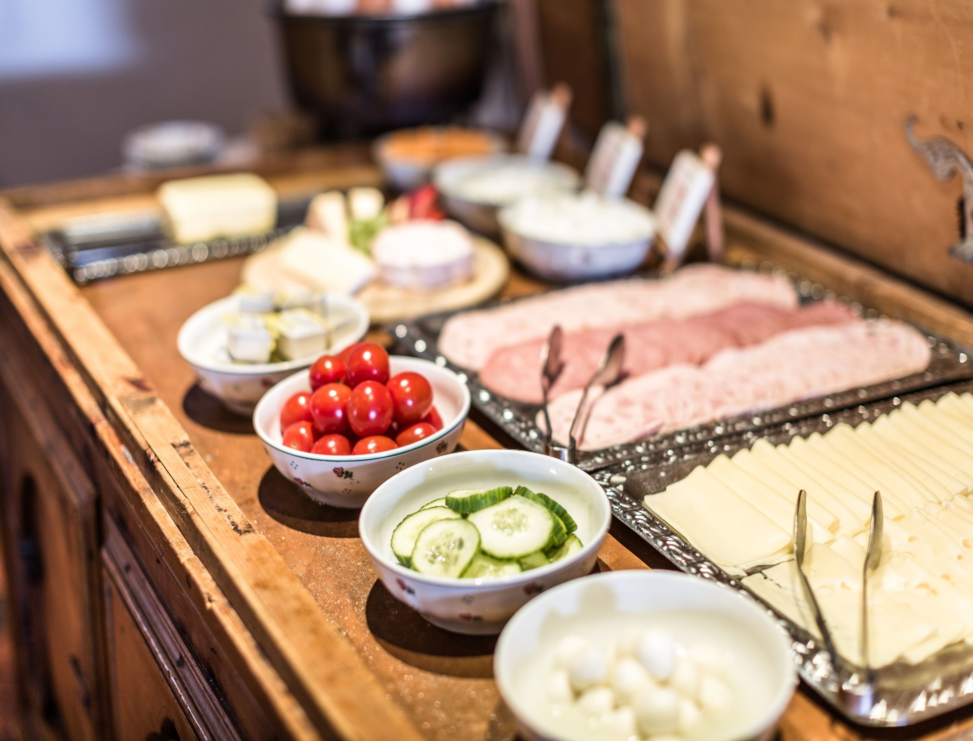 Ein reichhaltiges Buffet mit verschiedenen Speisen, darunter Gurkenscheiben, Kirschtomaten und Käse.