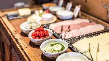 Ein reichhaltiges Buffet mit verschiedenen Speisen, darunter Gurkenscheiben, Kirschtomaten und Käse.