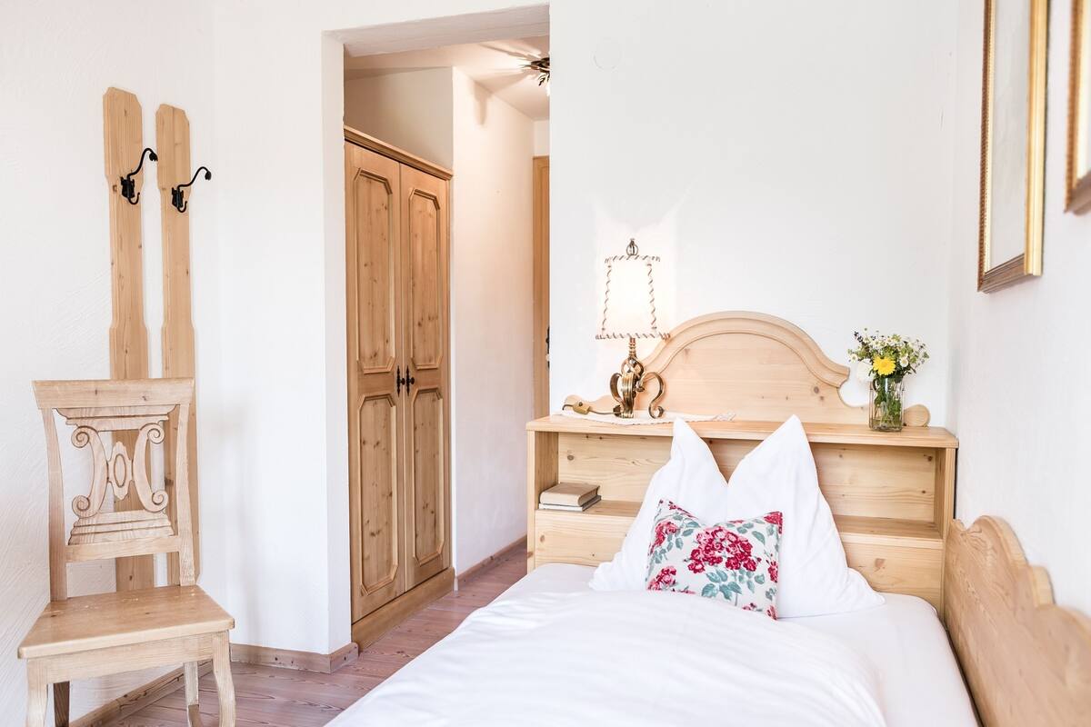 A bedroom with a wooden bed, a nightstand with a lamp, a chair, and a wardrobe.