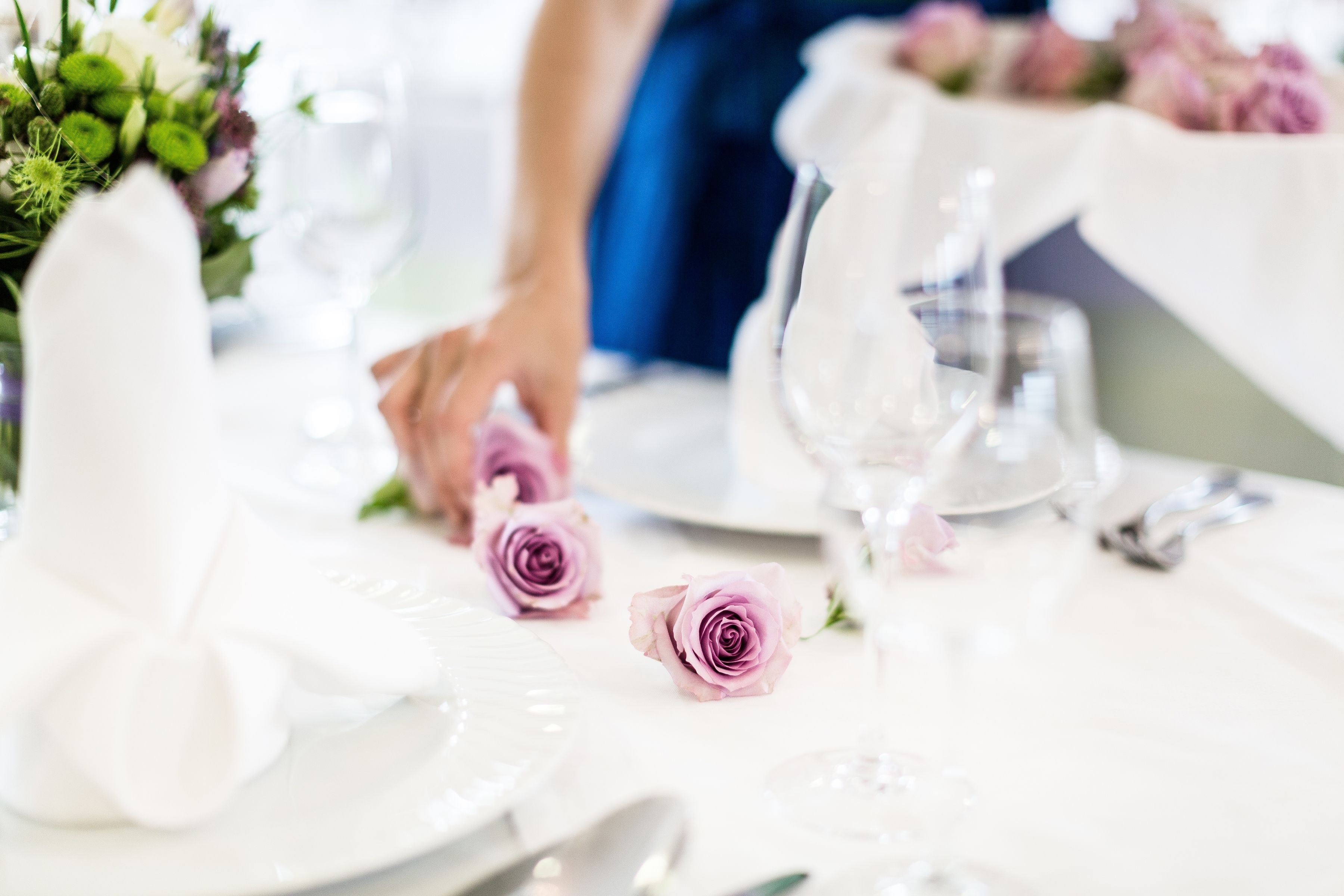 A table set with white plates, silverware, and pink roses.