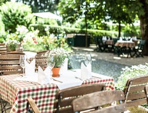 Un espace de restauration en plein air avec des tables pour deux personnes, agrémenté de nappes à carreaux et de plantes en pot.