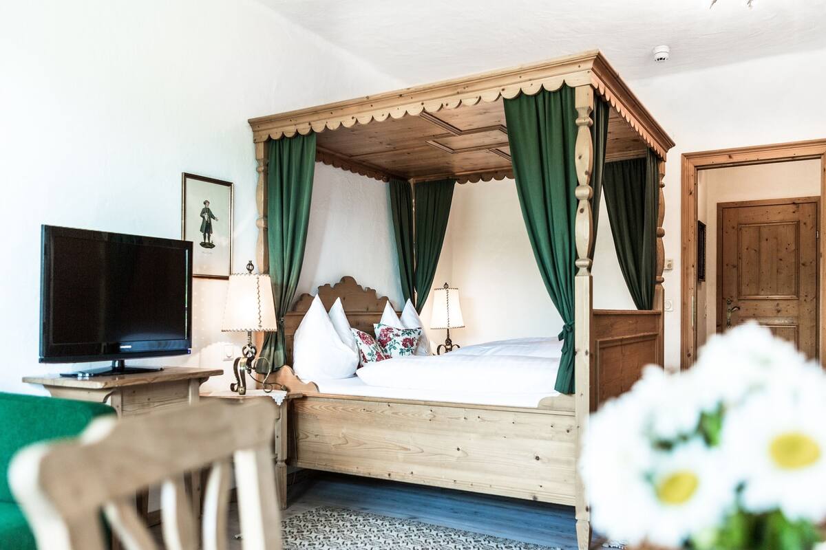 A four-poster bed with green curtains, a television on a wooden stand, and a framed picture on the wall.