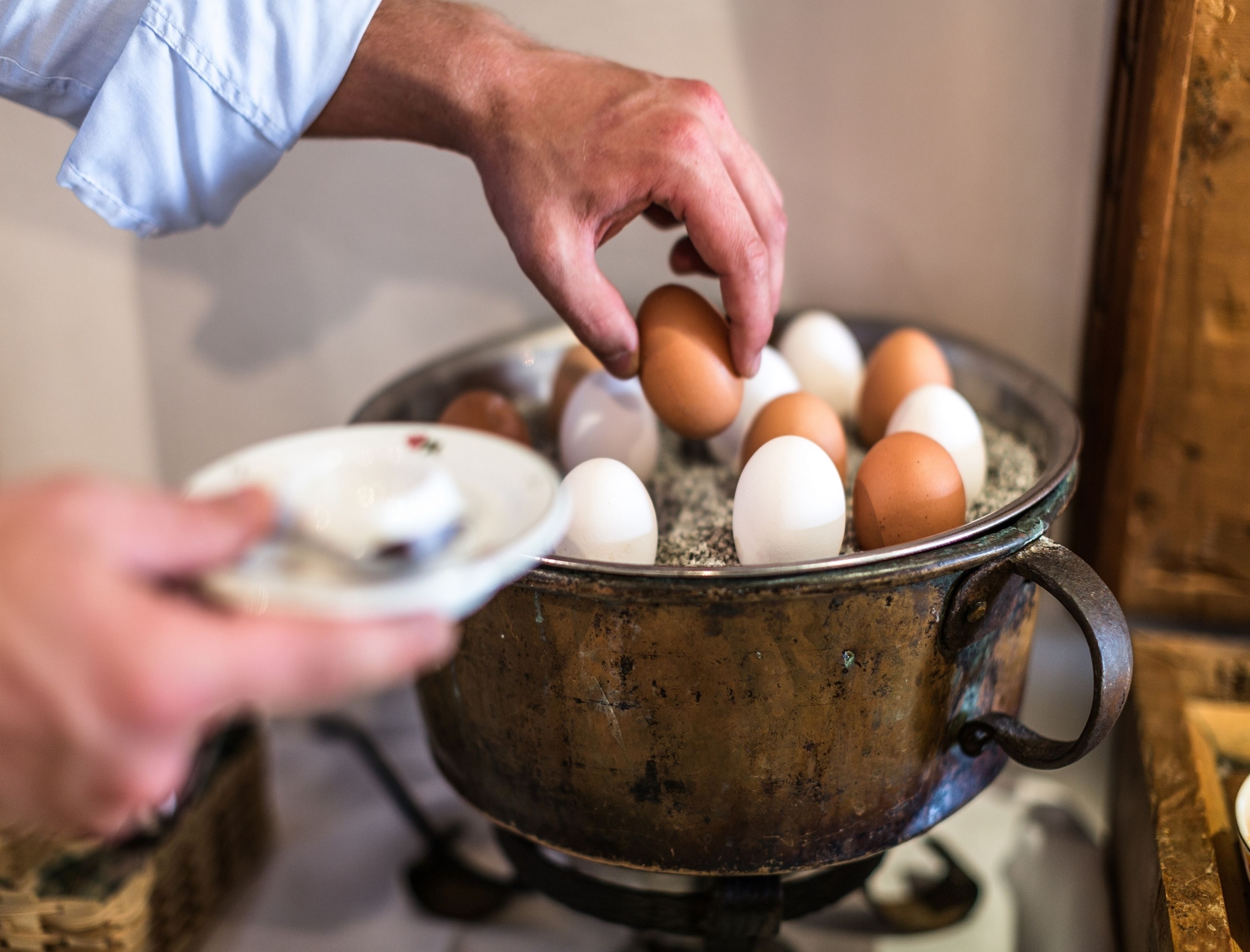 A person holding a plate with eggs, placing them into a pot.