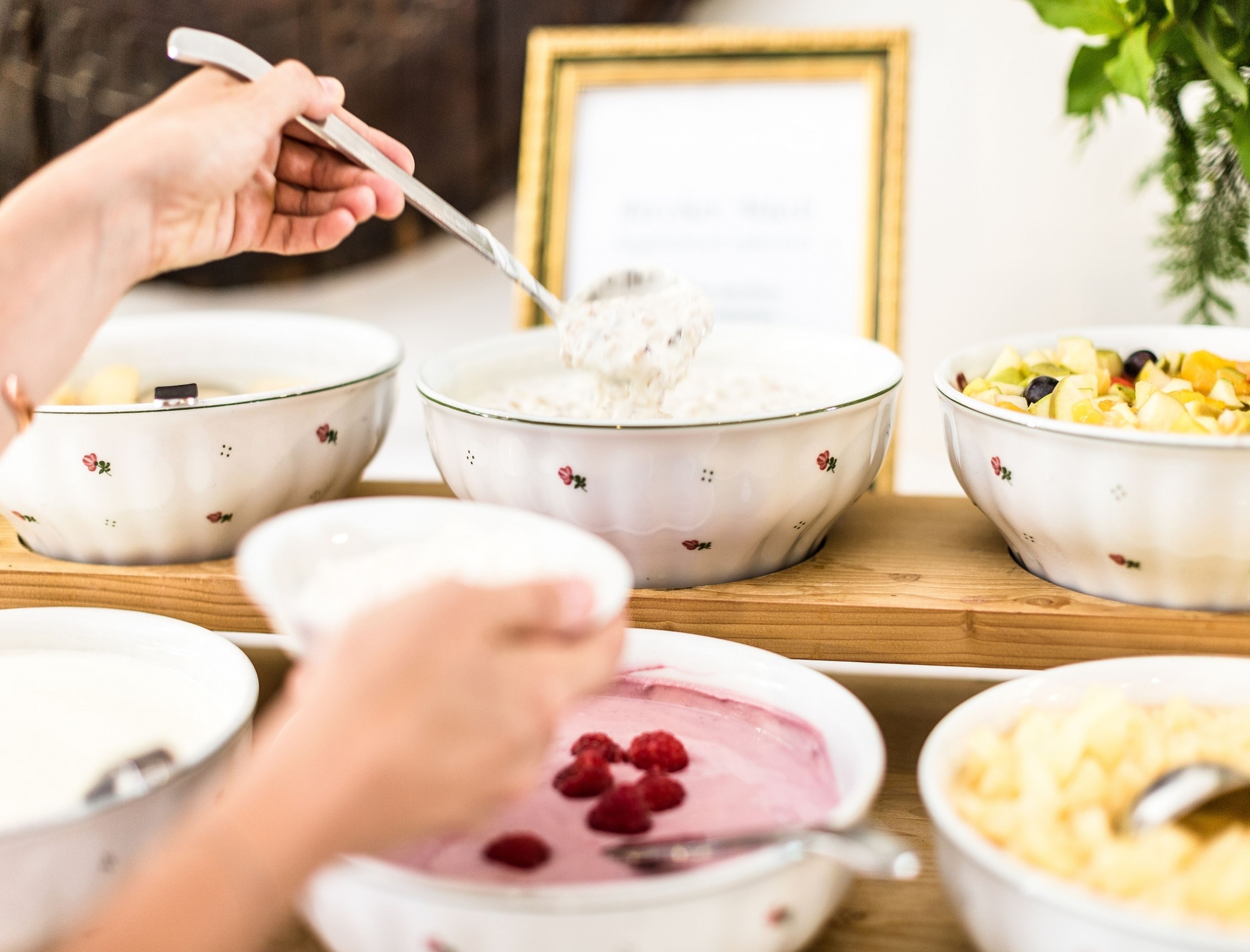 Ein Esstisch mit verschiedenen Schalen voller Speisen, darunter eine Joghurt-Schale mit Himbeeren, eine Obstsalat-Schale und eine Haferflocken-Schale.