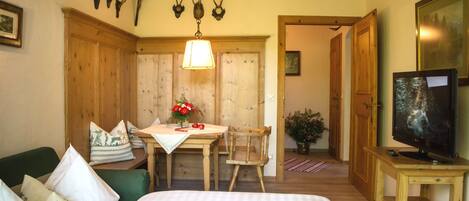 Una habitación con una cama, una mesa de comedor con sillas, un televisor sobre un mueble de madera y una puerta que da a otra habitación.