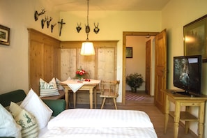 Une pièce comprenant un lit, une table à manger avec des chaises, un téléviseur posé sur un meuble en bois, et une porte donnant sur une autre pièce.