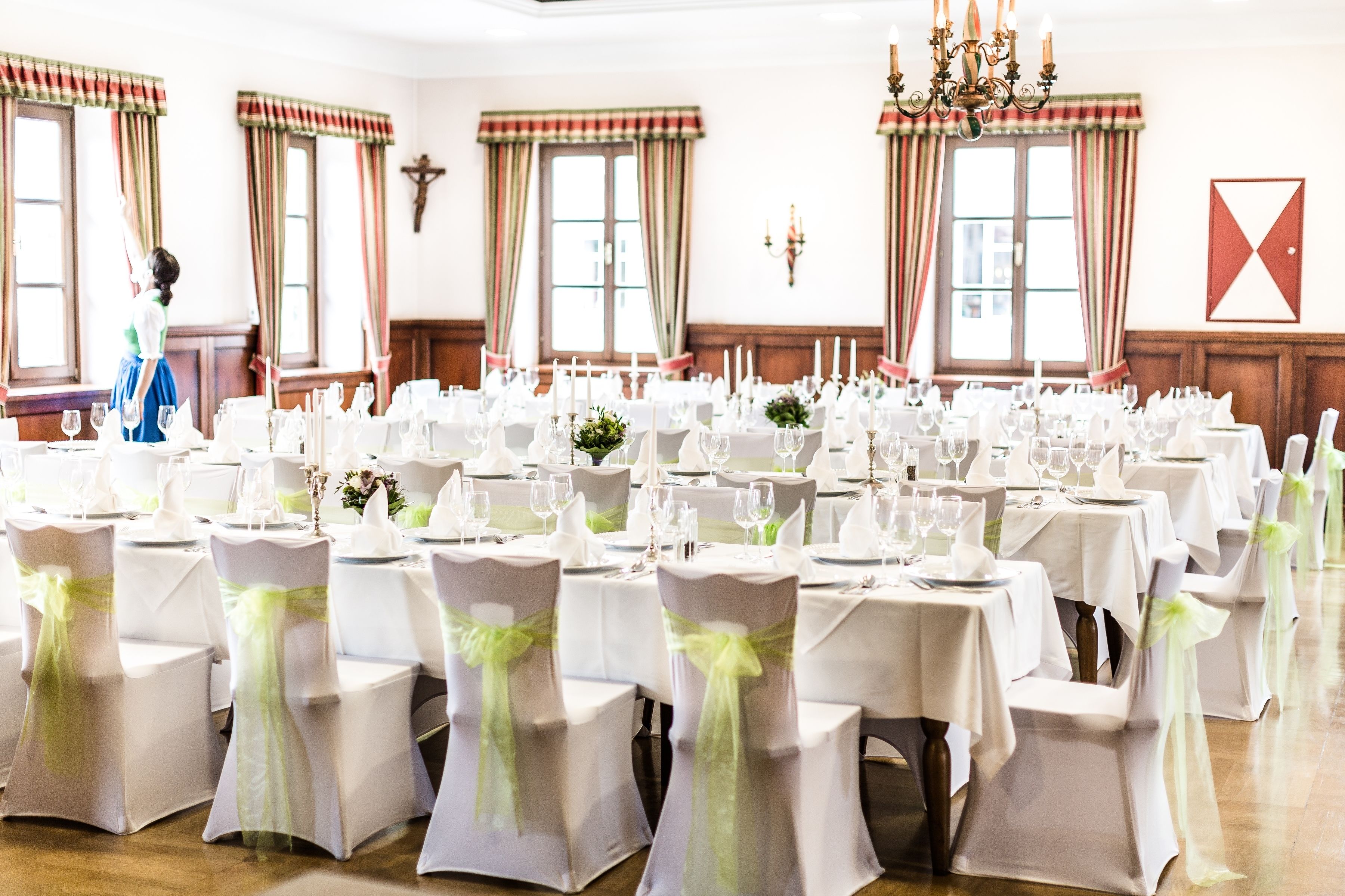 A banquet hall with multiple round tables set for a formal event, each with white tablecloths and green sashes.
