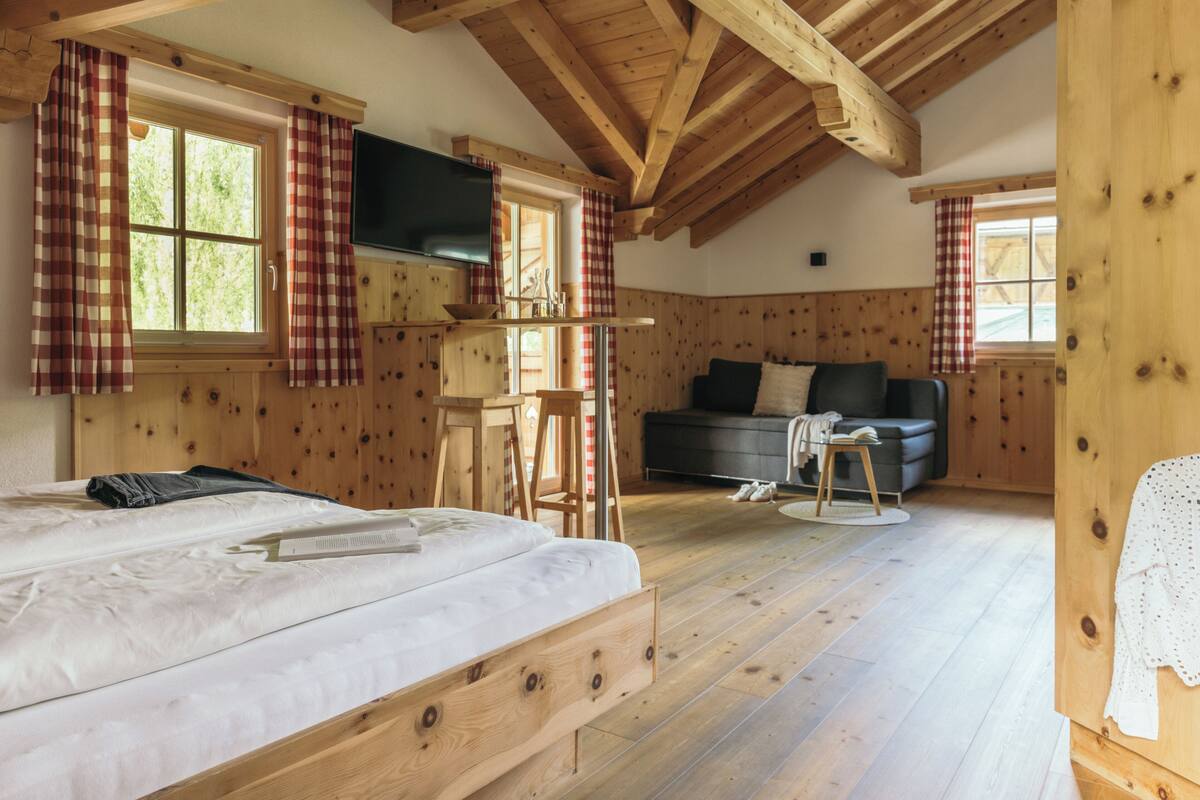 Een houten kamer met een bed, een bank, een televisie en een raam met gordijnen.