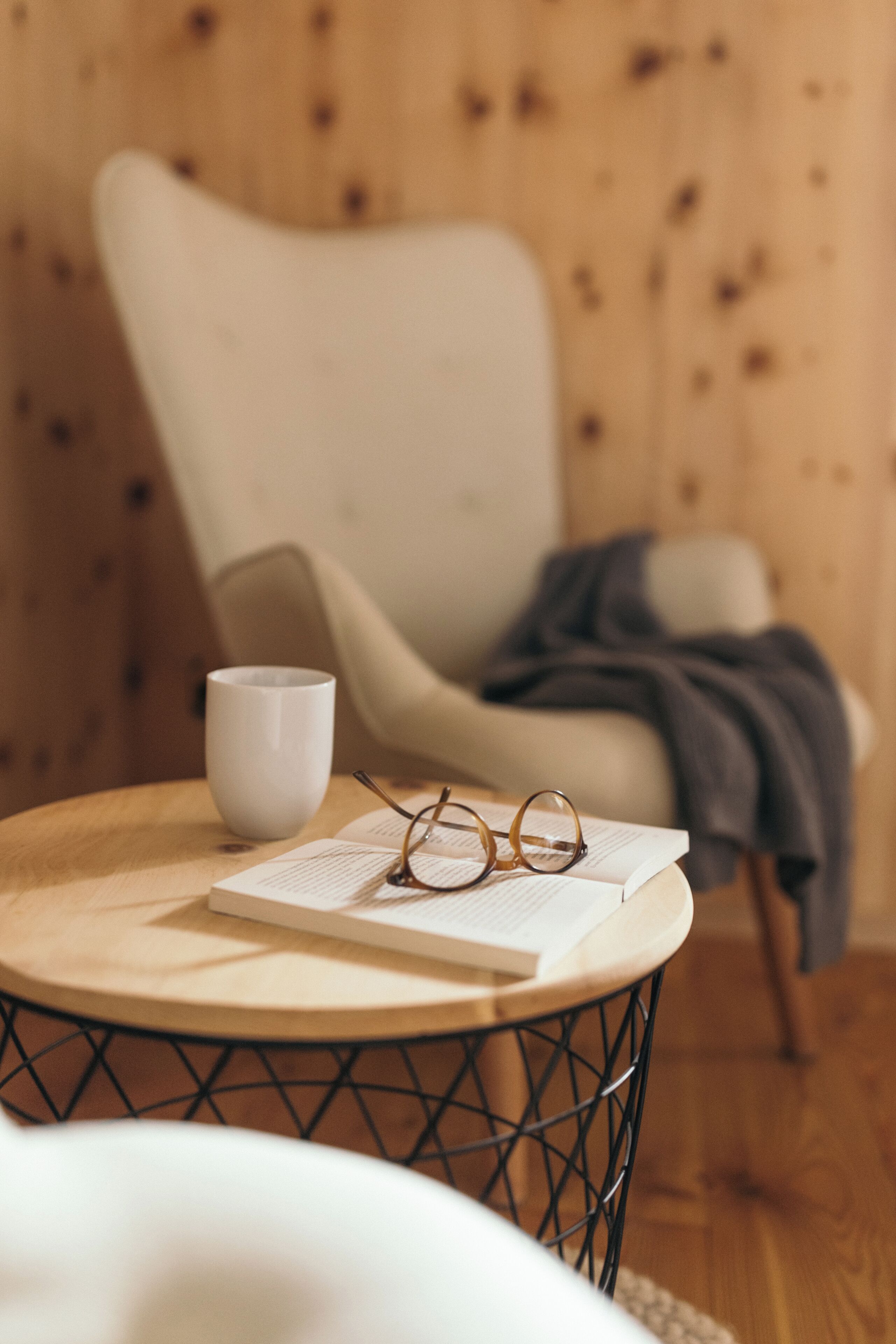 Una habitación acogedora con una mesa redonda de madera, una taza blanca y un par de gafas sobre un libro abierto.