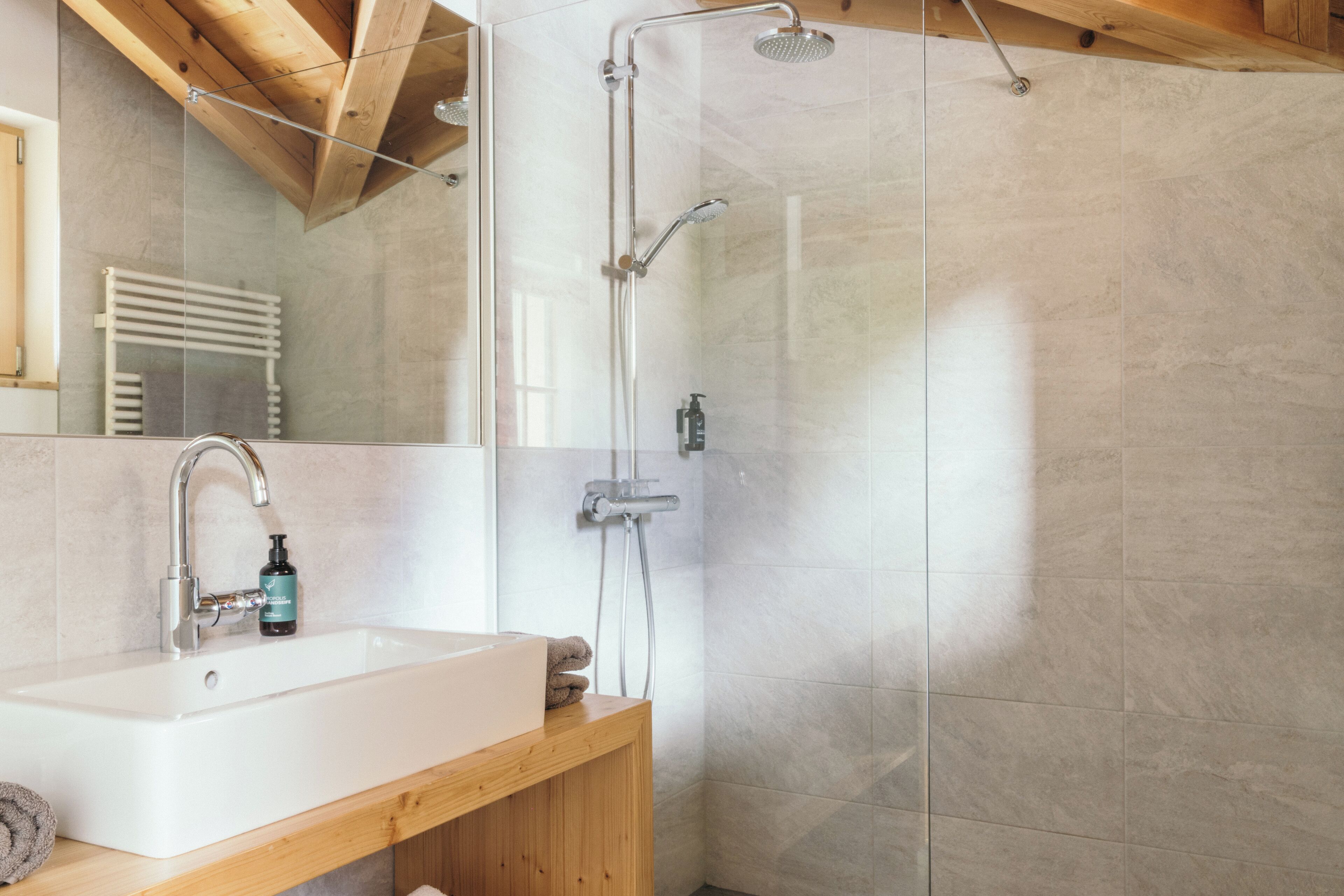A modern bathroom with a glass-enclosed shower, a white sink, and a wooden vanity.