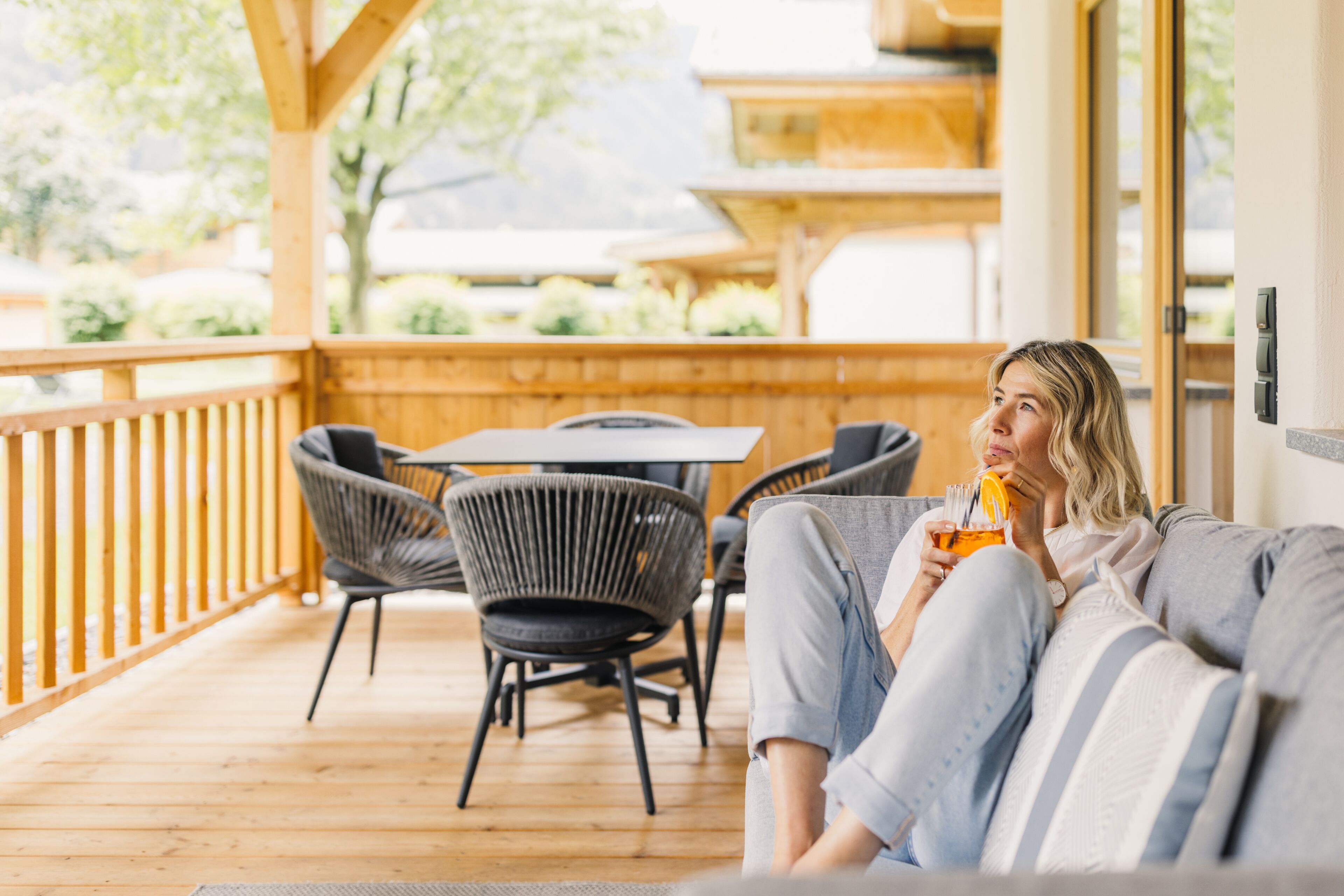 Una terraza de madera con sofá y sillones, una mesa y vistas al verdor.
