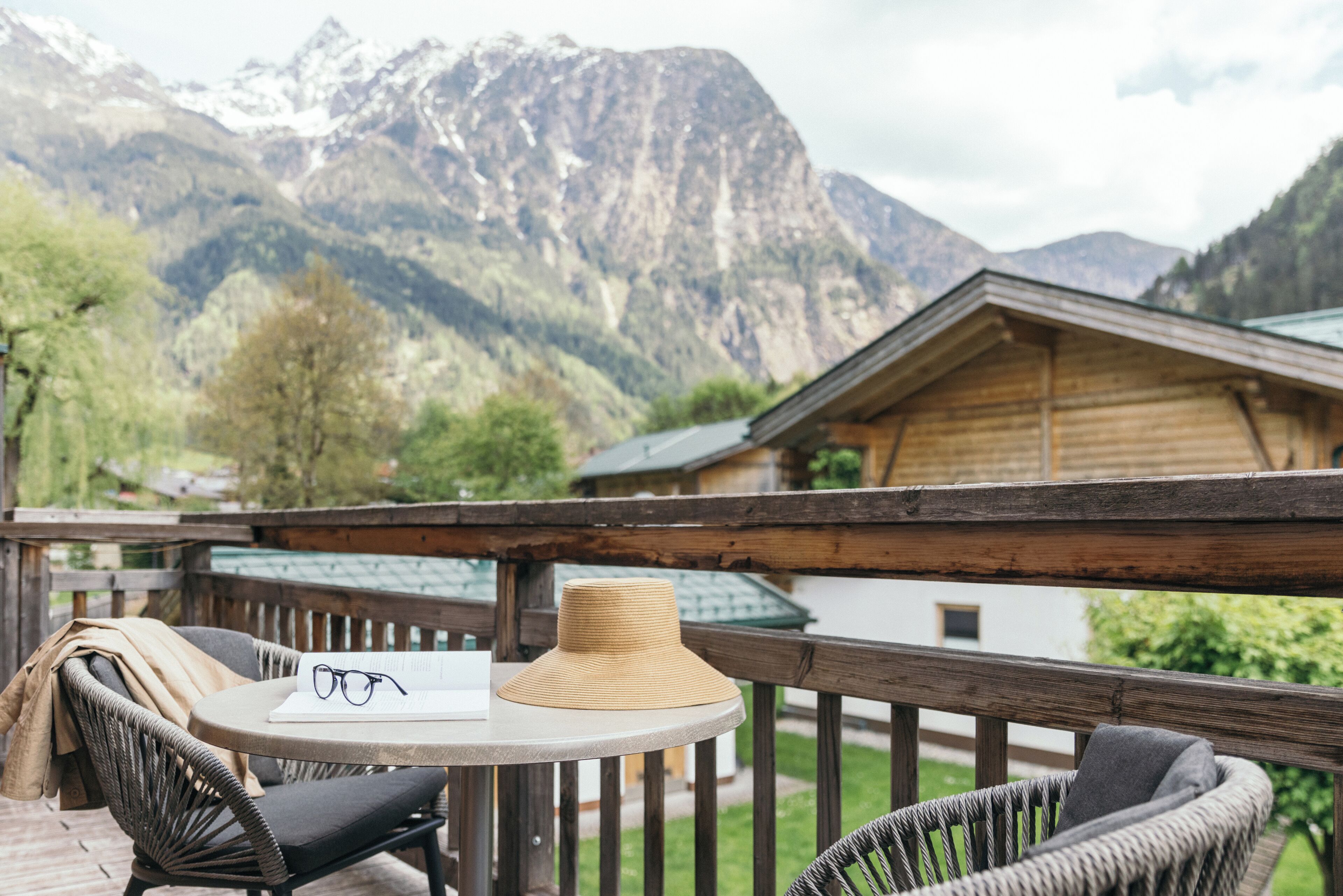 A wooden deck with wicker chairs and a table, overlooking a mountain range.