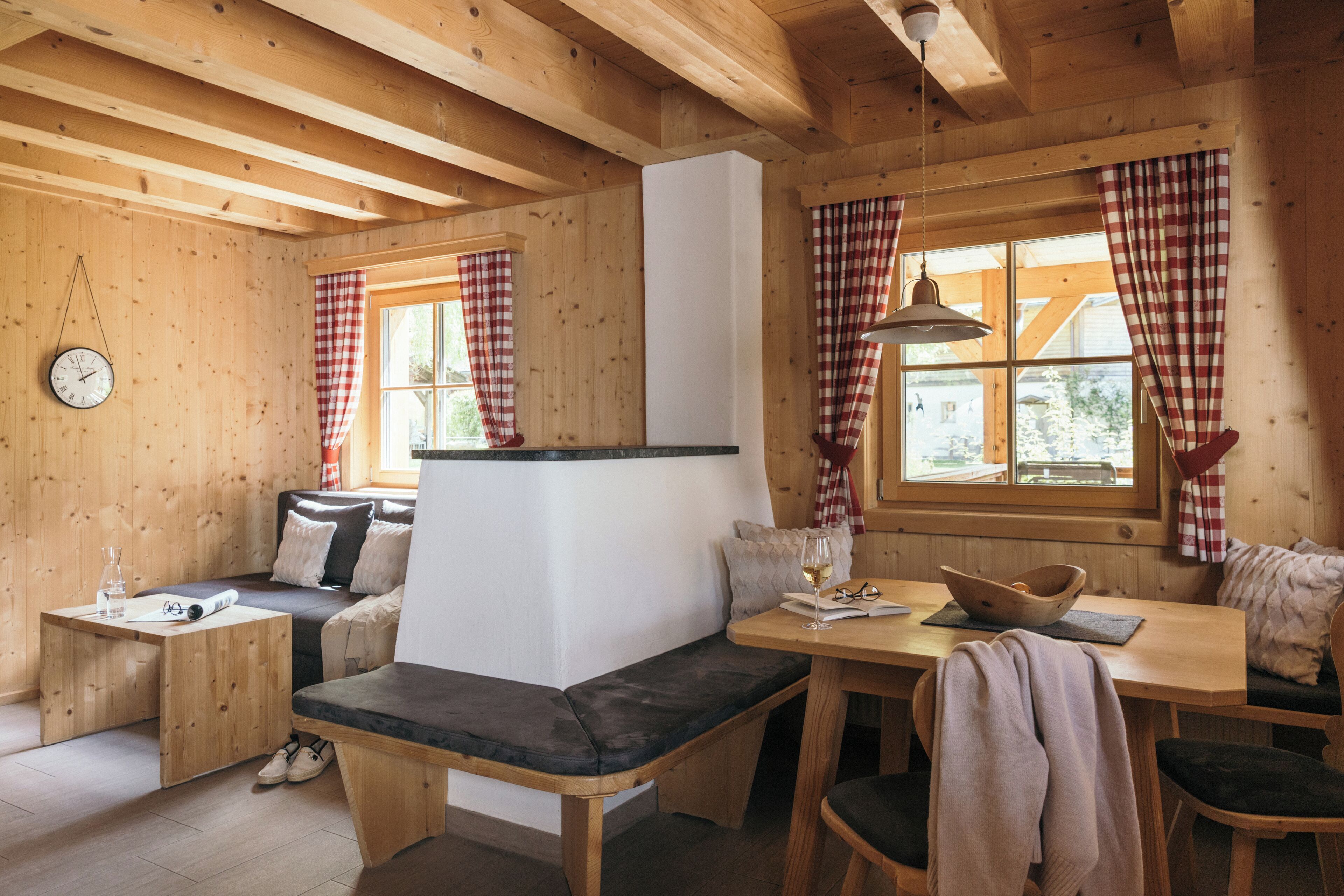 Un interior de cabaña acogedor con un banco de madera, una mesa de comedor y un reloj en la pared.