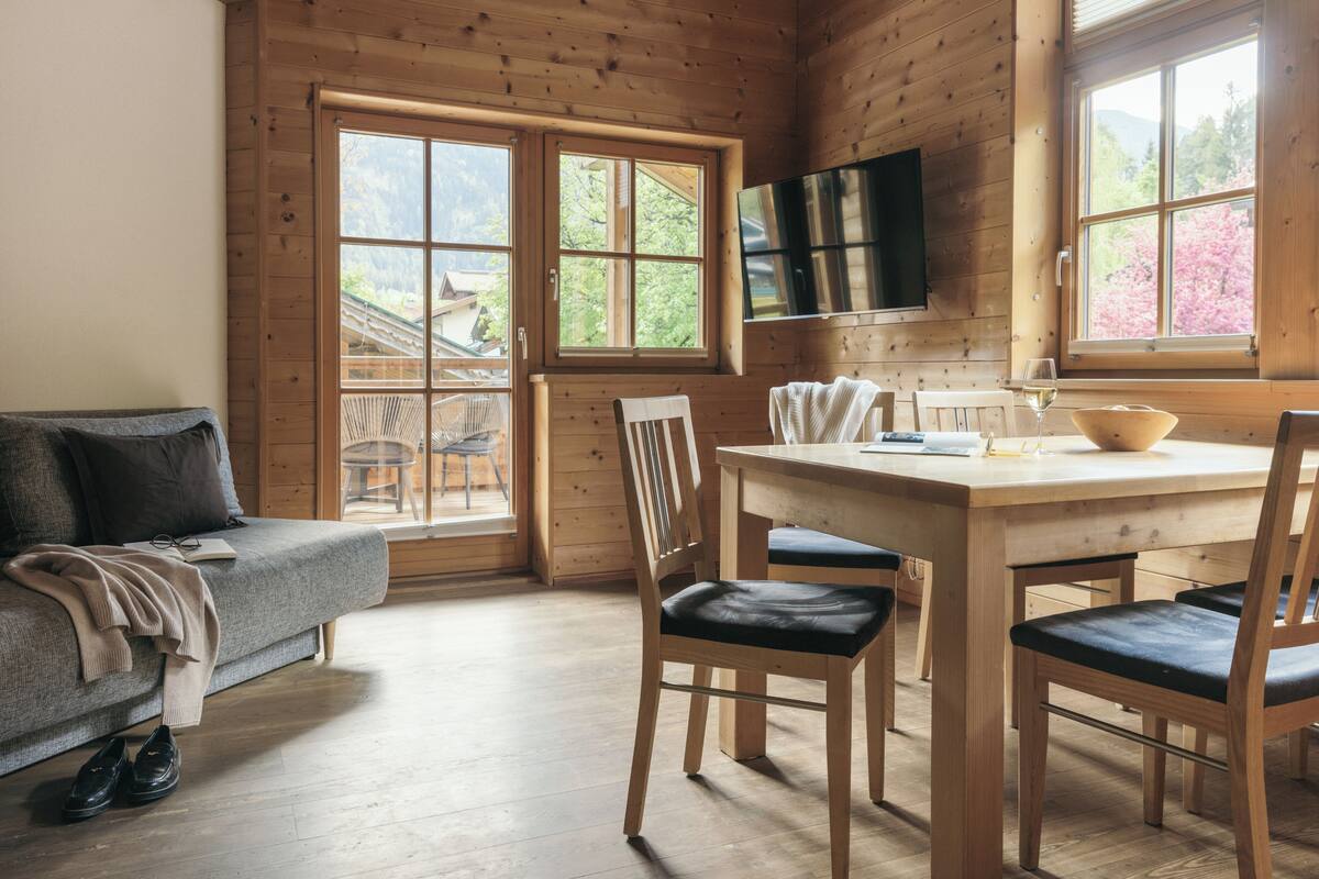 Een houten hut binnen met een bank, eettafel, stoelen en een aan de muur bevestigde televisie.