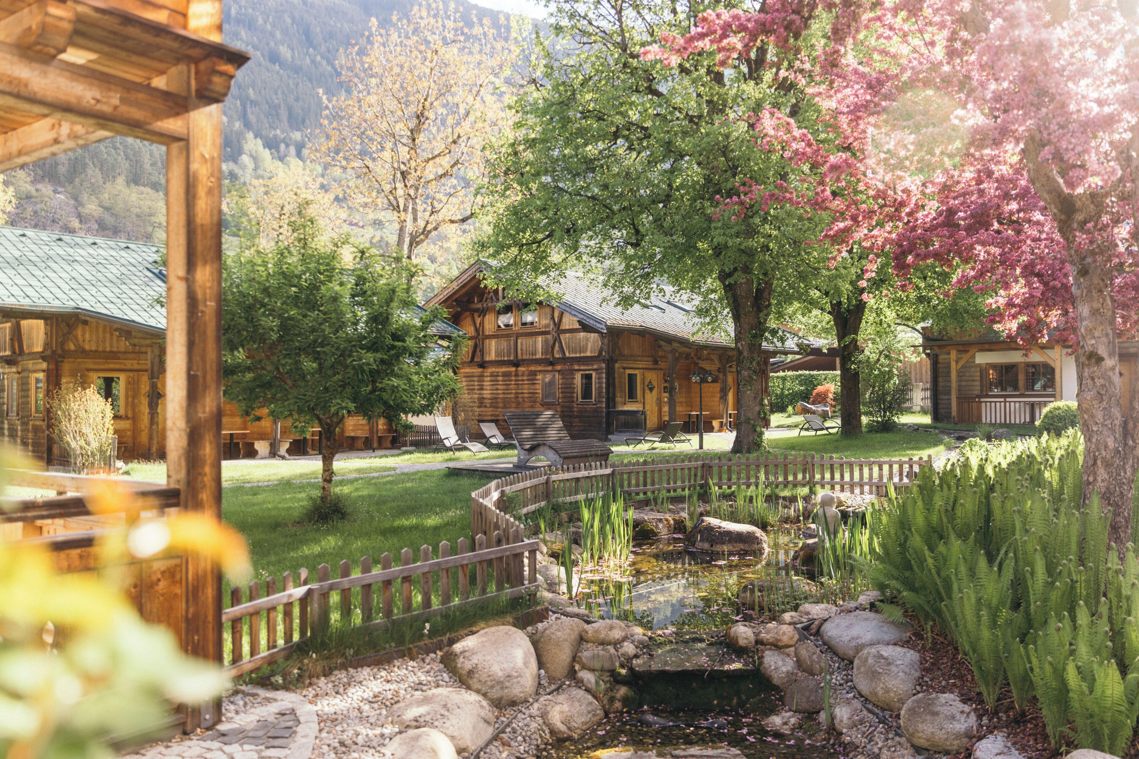 A wooden lodge with a pond, surrounded by a wooden fence and lush greenery.