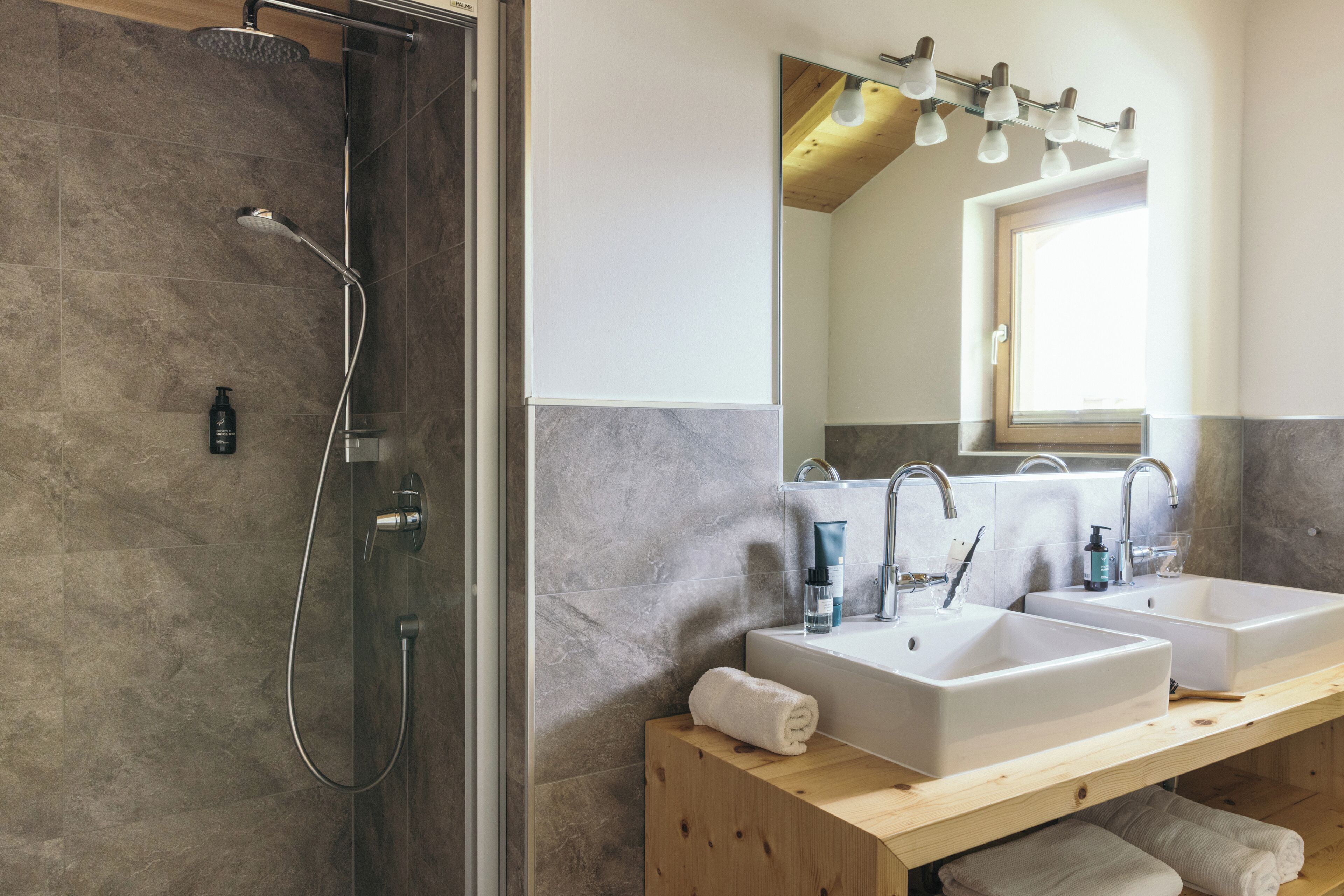 Un baño moderno con ducha de vidrio, dos lavamanos y tocador de madera.