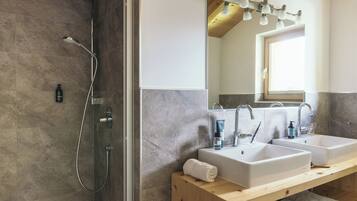 Un baño moderno con ducha de vidrio, dos lavamanos y tocador de madera.