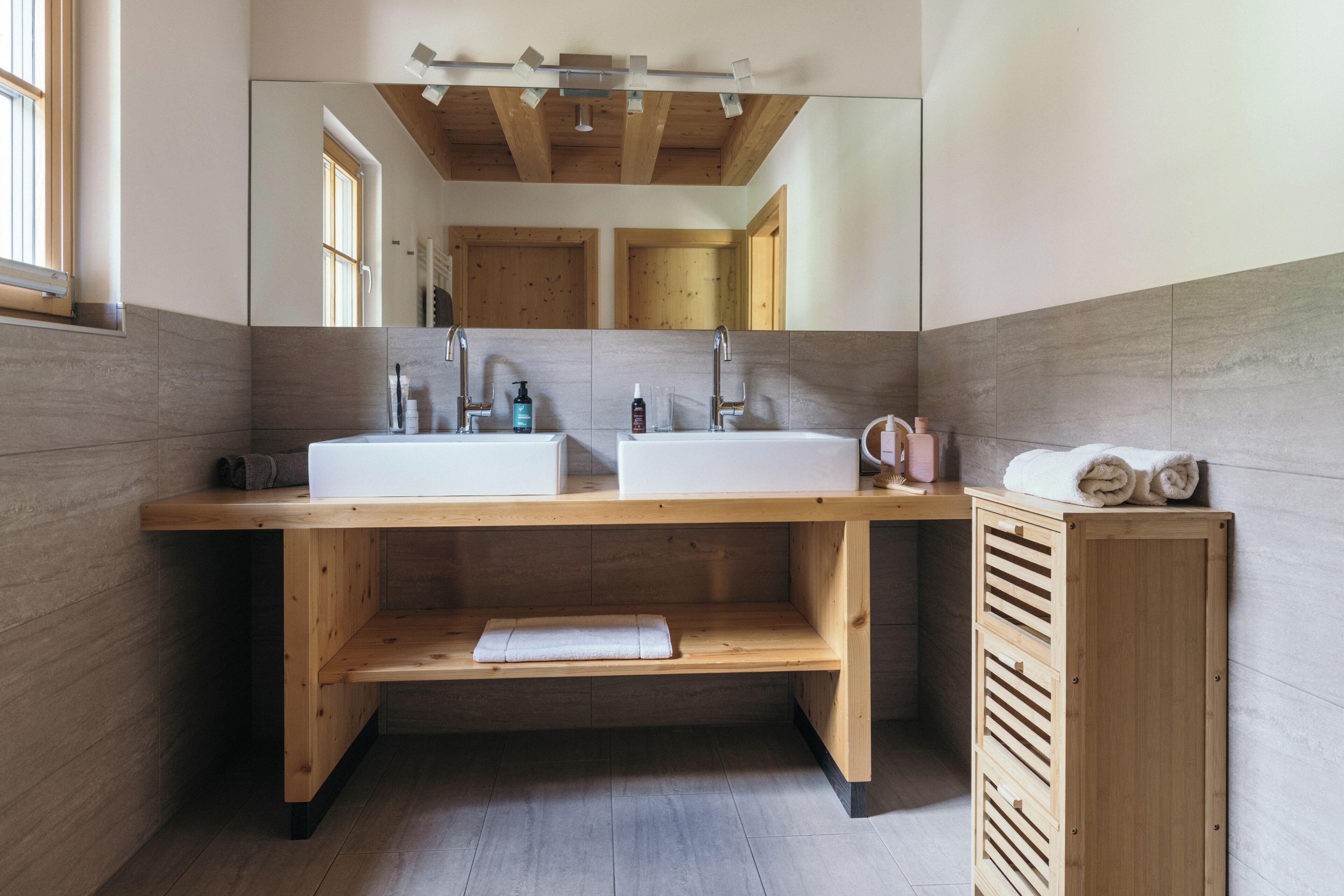 A modern bathroom with two sinks, wooden vanity, and a large mirror.
