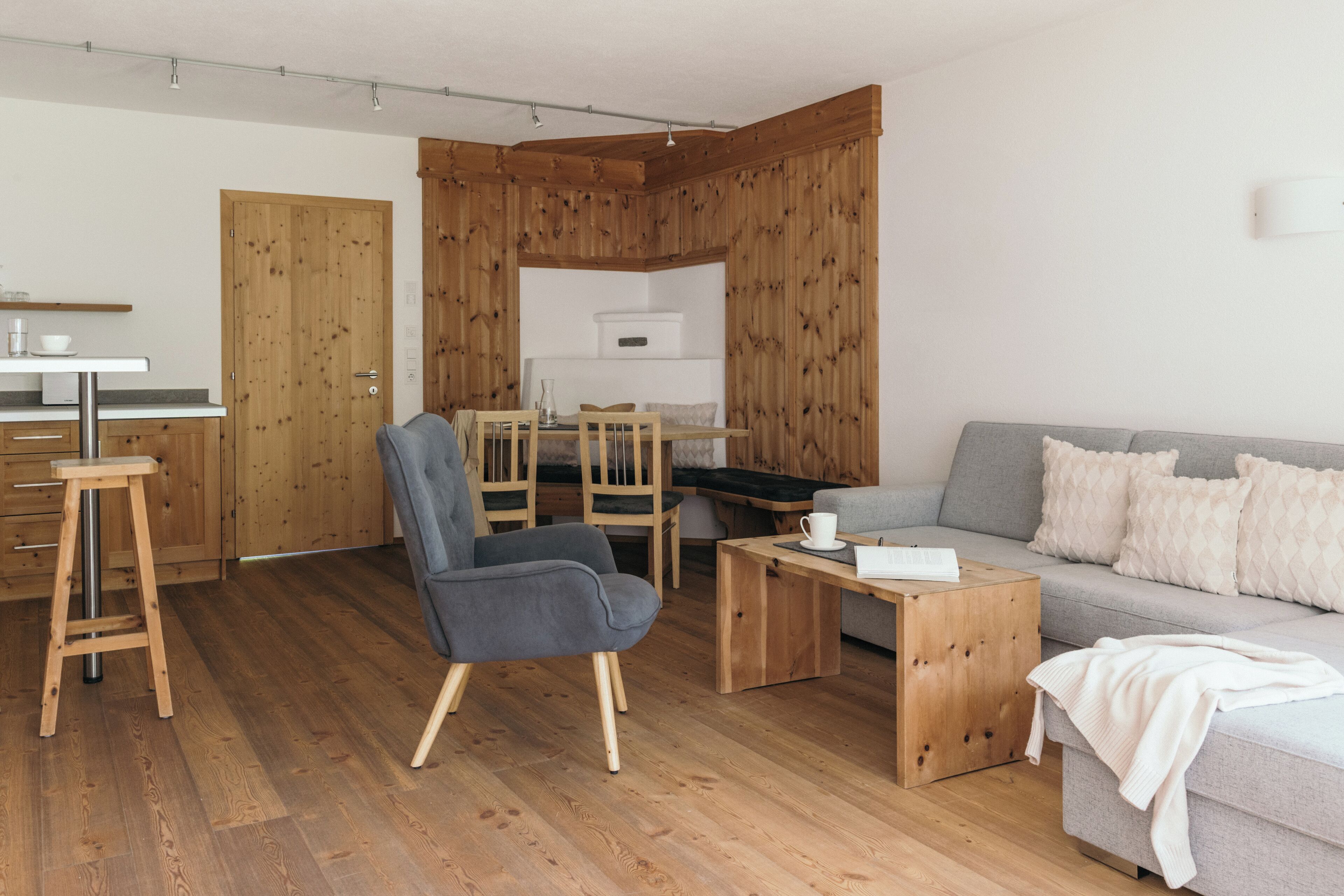 Ein modernes Wohnzimmer mit einem grauen Sofa, Holzboden und einem Essbereich mit Tisch und Stühlen.