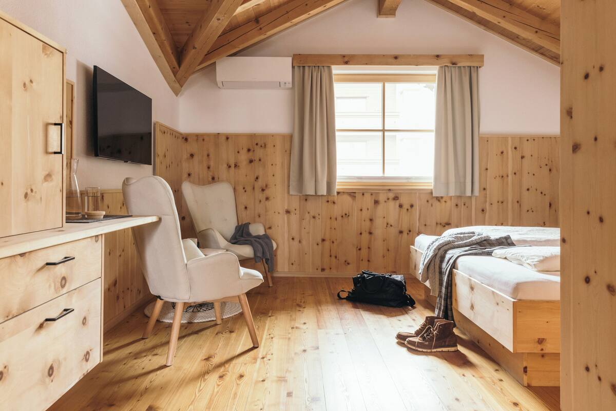 Een kamer met houten lambrisering, een bed, een bureau, een stoel, een televisie en een raam met gordijnen.