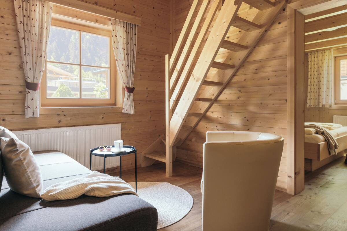 Een gezellige kamer met een bed, een stoel, een klein tafeltje, een raam met gordijnen en een houten trap.