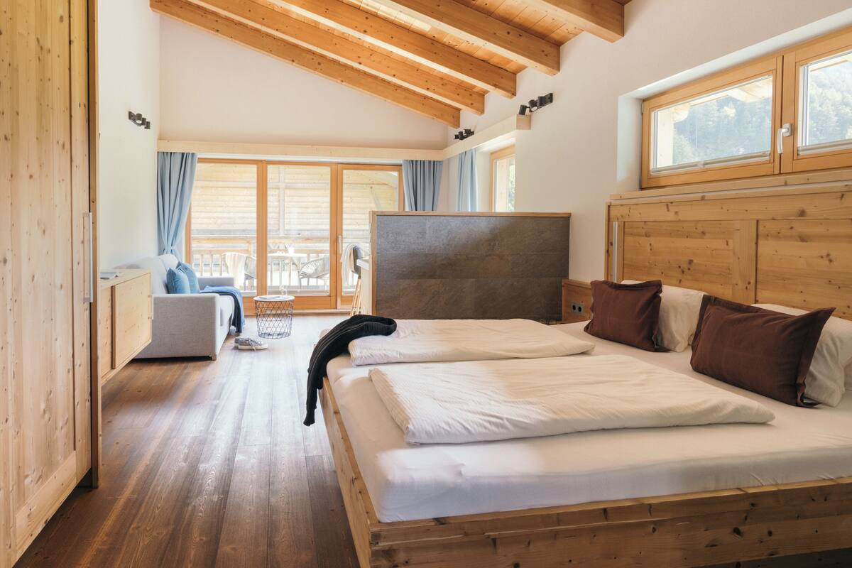 Een slaapkamer met houten frame, een groot bed, een zithoek en een balkon met uitzicht.