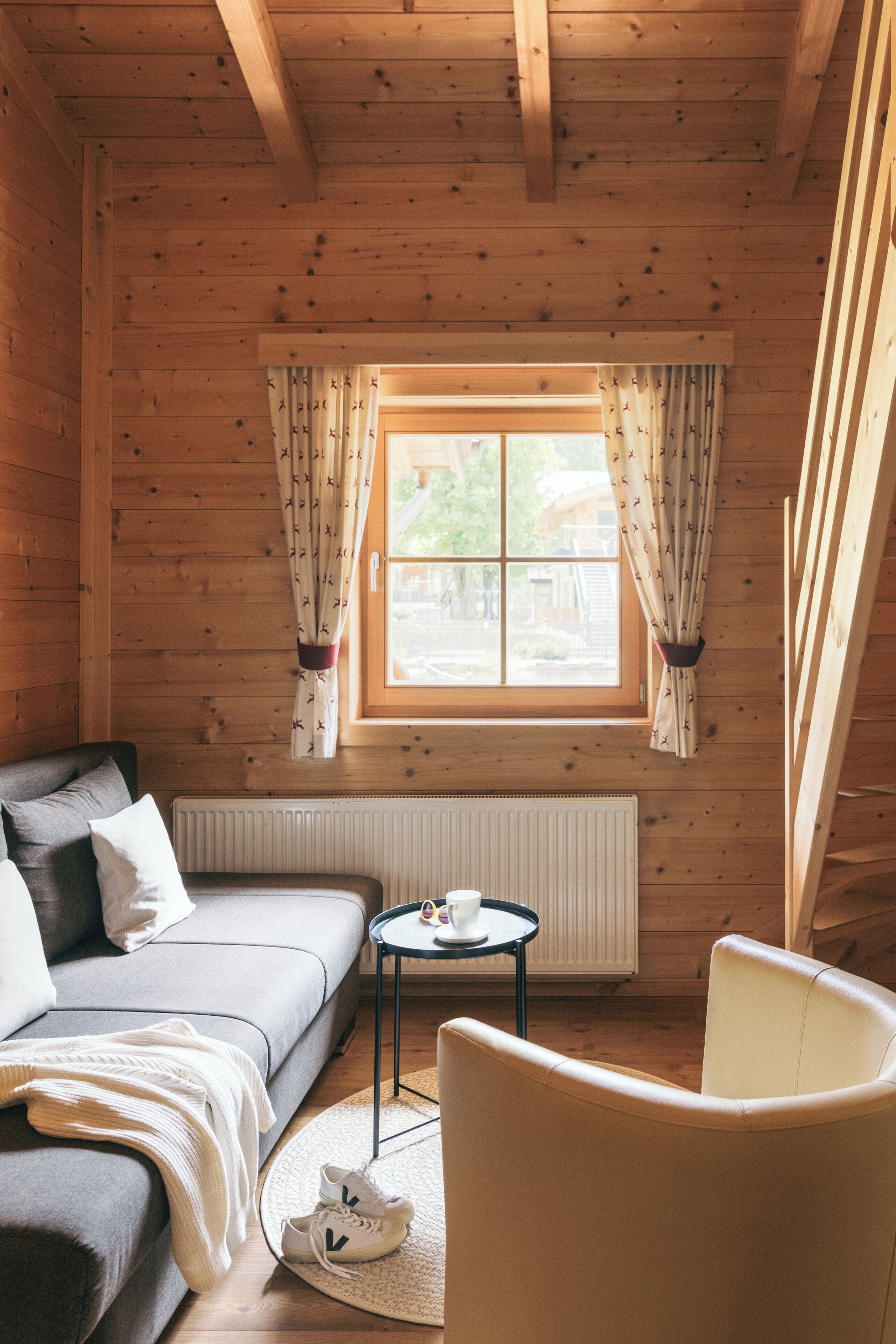 A cozy wooden cabin room with a sofa, a small round table with a cup, and a chair.