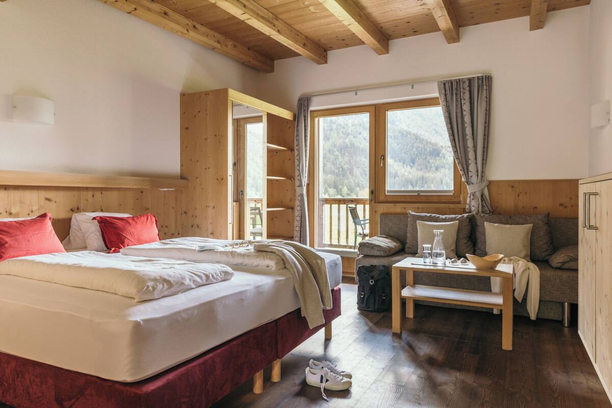 Een knus ingerichte kamer met een bed, een bank, een kleintje tafeltje en een raam met gordijnen.