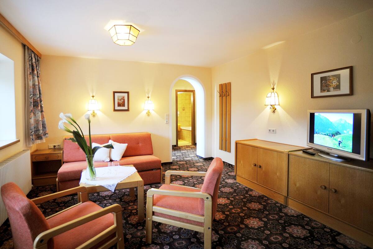 A hotel room with a sofa, chairs, a small table, a TV, and a decorative plant.
