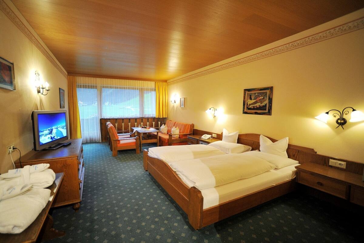 A hotel room with a bed, a desk with a chair, a television, and a window with curtains.